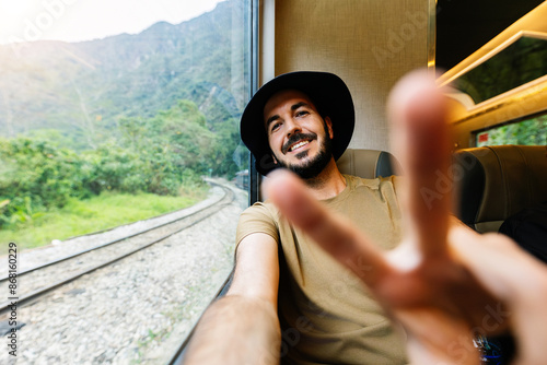 Young happy man traveling by train during summer vacation. Joyful male taking selfie on Peru tourist rail train travel from Ollantaytambo to Machu Picchu. Adventure concept. photo