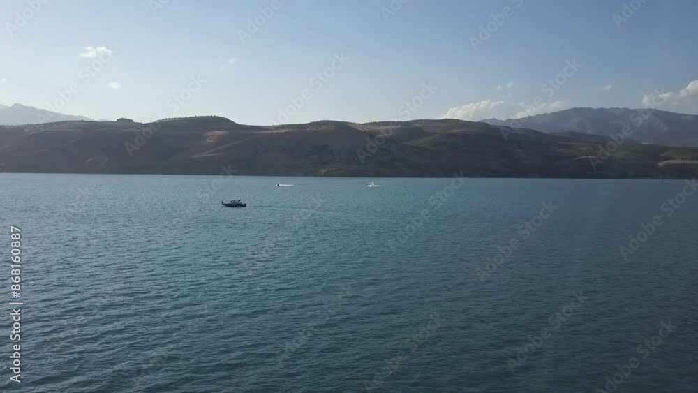 A drone flies over the lake among the mountains. A boat and a jet ski float on the water. A sunny summer day. A drone flies over the lake among the mountains. A boat and a jet ski float on the water. A sunny summer day.