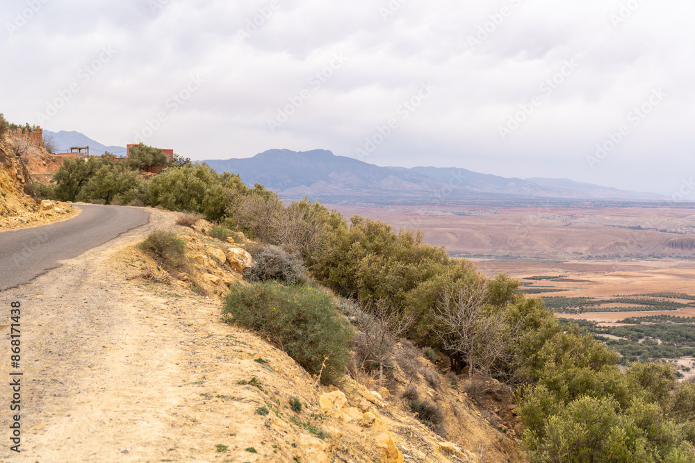 Fototapeta premium Arid Moroccan landscape near Marrakech, sparse vegetation, rolling hills, dry terrain, distant mountains