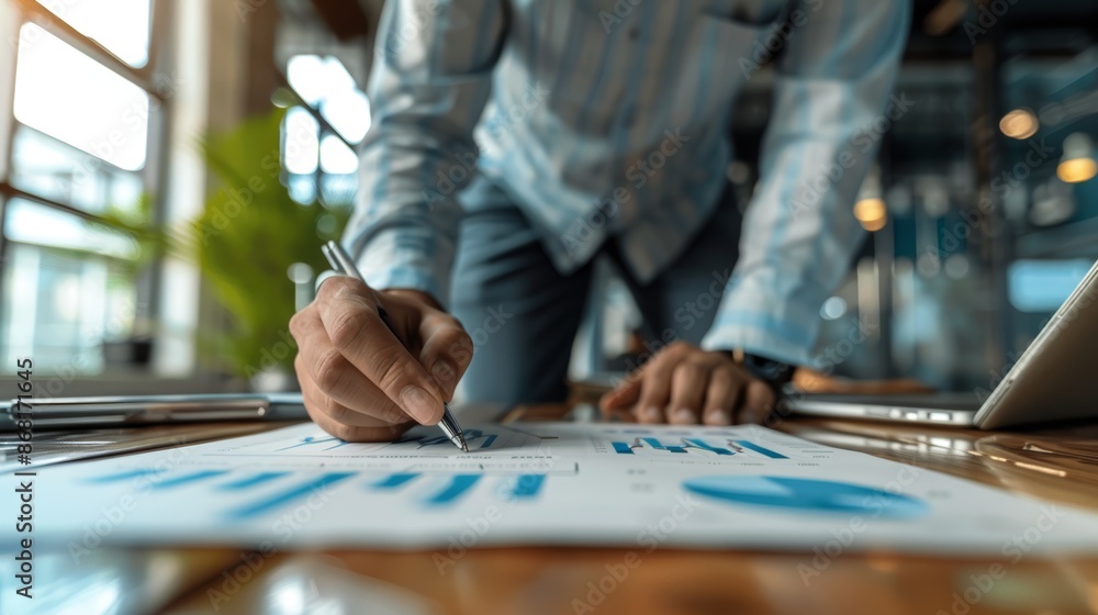 A businessman working on a desk, analyzing financial graphs and charts with a pen. A businessman working on a desk, analyzing financial graphs and charts with a pen.