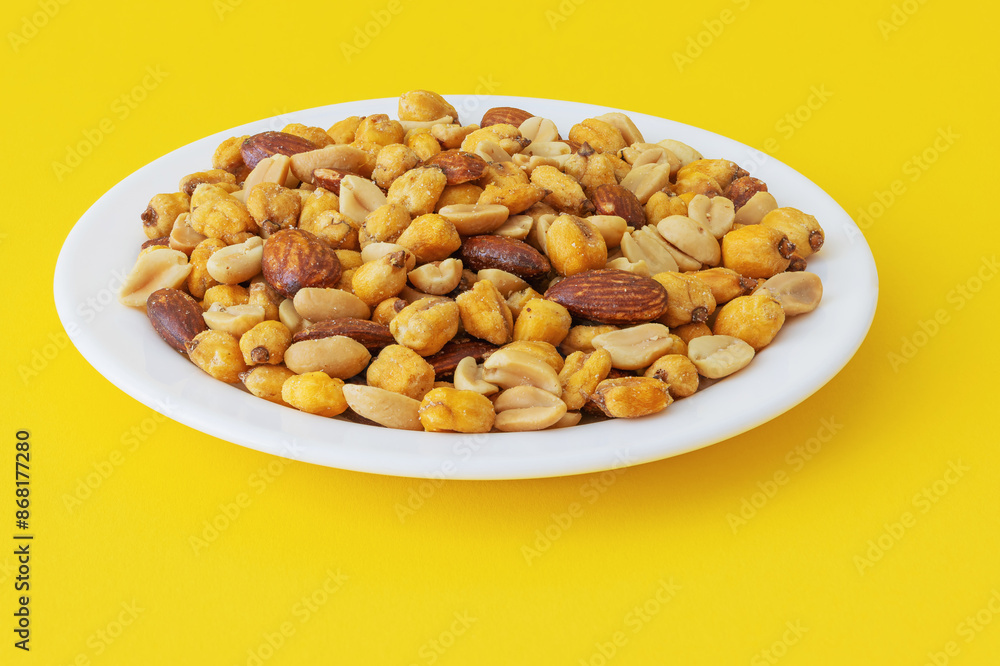 Roasted peanuts, corn and almonds in a plate on a yellow background Roasted peanuts, corn and almonds in a plate on a yellow background