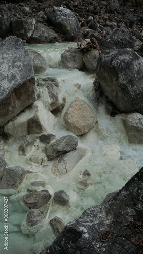 A clear river with hot sulfur water flows through the rugged landscape of the Sorikmarapi volcano area, North Sumatra, Indonesia. photo