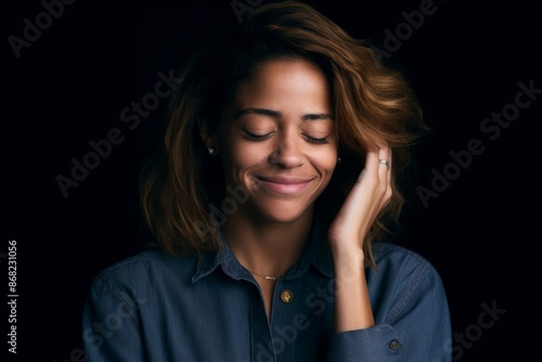 portrait of smiling woman with closed eyes and hand on her face in front of black background
