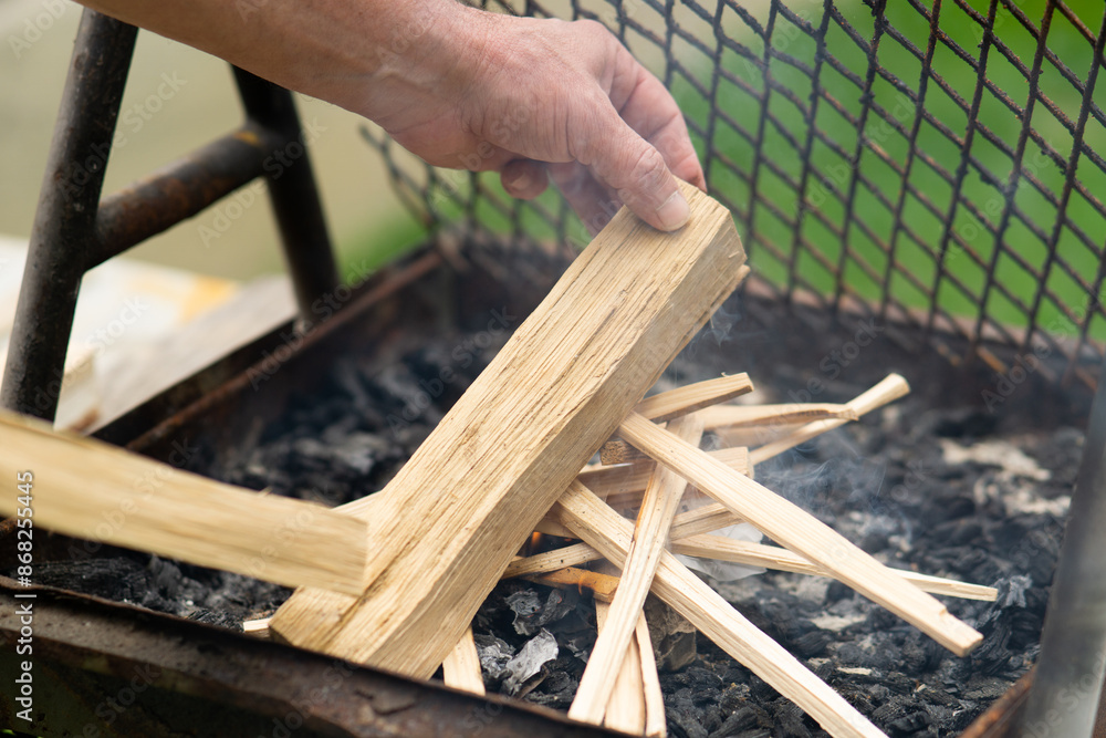 A man light a fire on an outdoor grill using wood sticks, preparing fire for a barbecue. garden setting. A man light a fire on an outdoor grill using wood sticks, preparing fire for a barbecue. garden setting.
