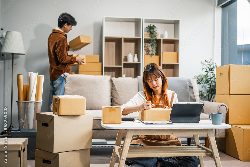 A young couple works from home, packing orders and managing their online store. They use technology and teamwork to run their business, smiling while fulfilling customer orders.