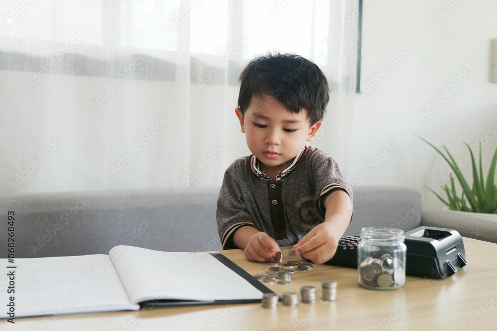 Little boy is saving money, counting coins and putting them in a glass jar. He learned to save money for his education and to buy things he wanted in the future. Little boy is saving money, counting coins and putting them in a glass jar. He learned to save money for his education and to buy things he wanted in the future.
