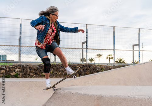 A graceful and assured senior woman with silver hair skateboarding in the open air. photo