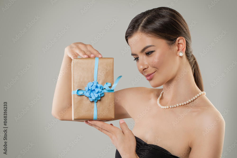 Nice model woman holds gift box in her hands and looks at present on gray background Nice model woman holds gift box in her hands and looks at present on gray background