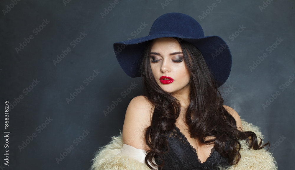 Attractive fashion model woman with long dark wavy hairstyle and red lips make-up wearing fashionable hat beauty studio portrait Attractive fashion model woman with long dark wavy hairstyle and red lips make-up wearing fashionable hat beauty studio portrait