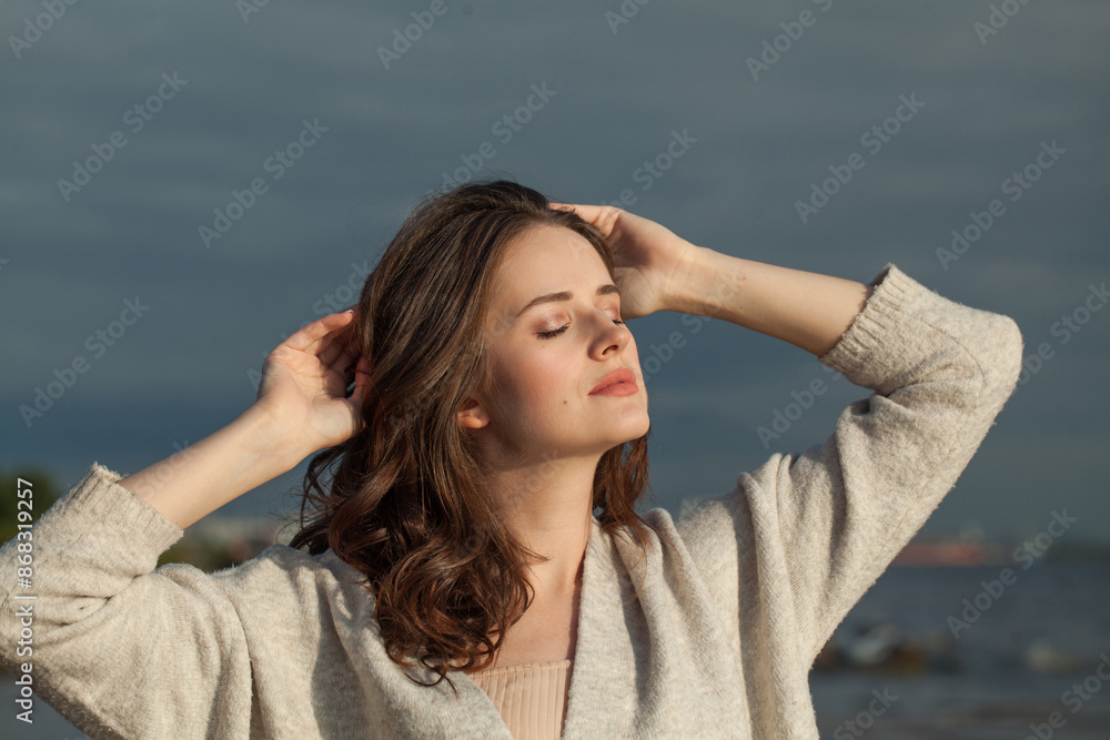 Smiling young woman model with brown hair and natural make-up walking along the shore of the resort on a spring morning. Happiness, balance, tranquility, emotion and mood concept Smiling young woman model with brown hair and natural make-up walking along the shore of the resort on a spring morning. Happiness, balance, tranquility, emotion and mood concept