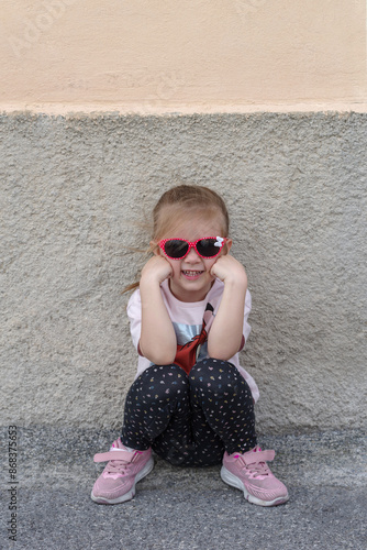 Girl sitting against a wall with sunglasses photo