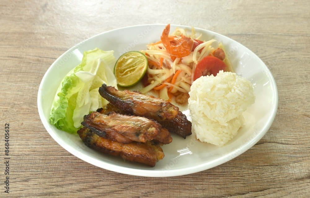 Som tum Thai spicy green papaya salad with roasted chicken wing eat couple sticky rice on plate Som tum Thai spicy green papaya salad with roasted chicken wing eat couple sticky rice on plate