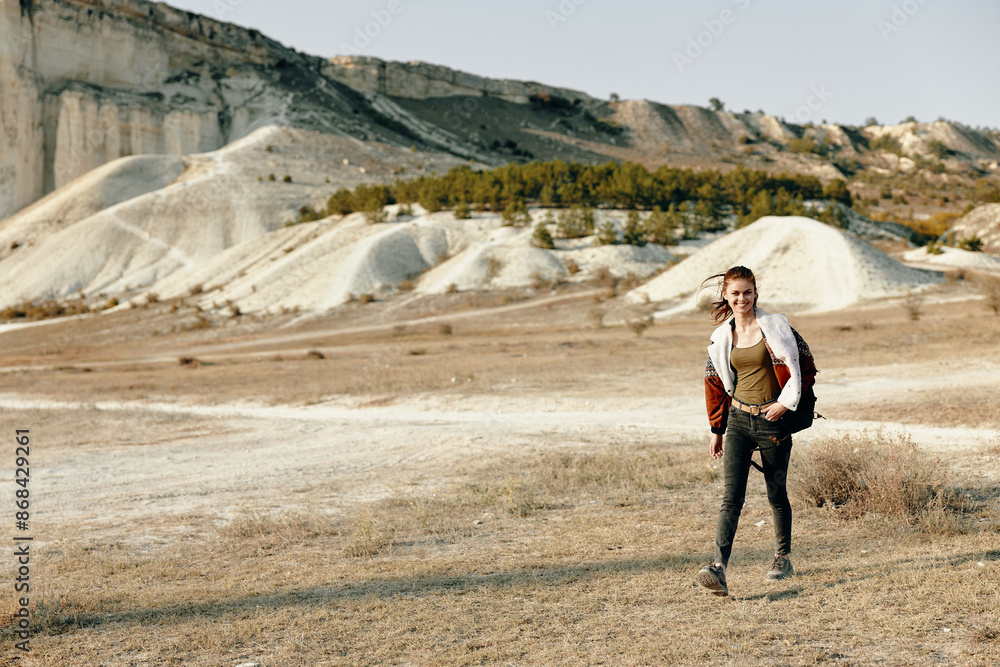 Obraz premium Serene woman walking through vast field with mountains, carrying a backpack