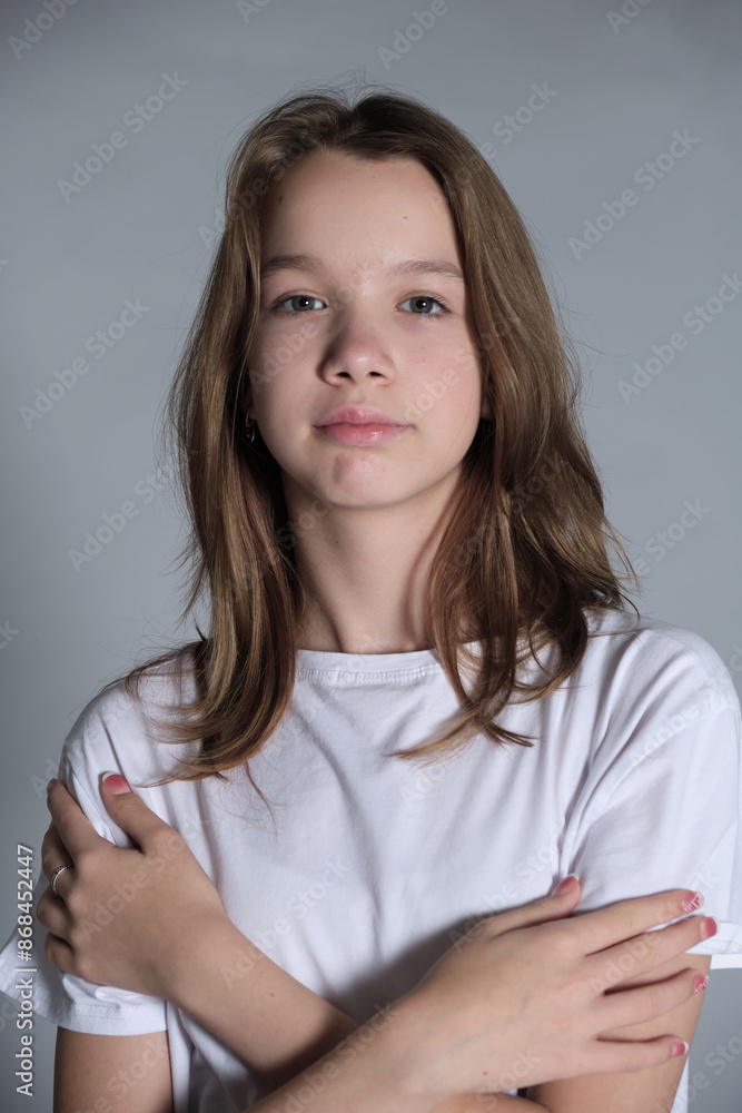 A young girl in a white t shirt crosses her arms and looks directly at the camera with a calm expression. This image highlights the confidence and self-assurance of youth in a modern context. A young girl in a white t shirt crosses her arms and looks directly at the camera with a calm expression. This image highlights the confidence and self-assurance of youth in a modern context.