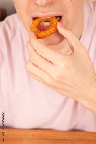 Caucasian man eats fresh fried onion rings with his hands, American fast food culture