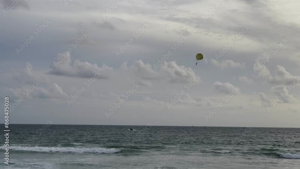Person parasailing at sunset over ocean island in background Person parasailing at sunset over ocean island in background