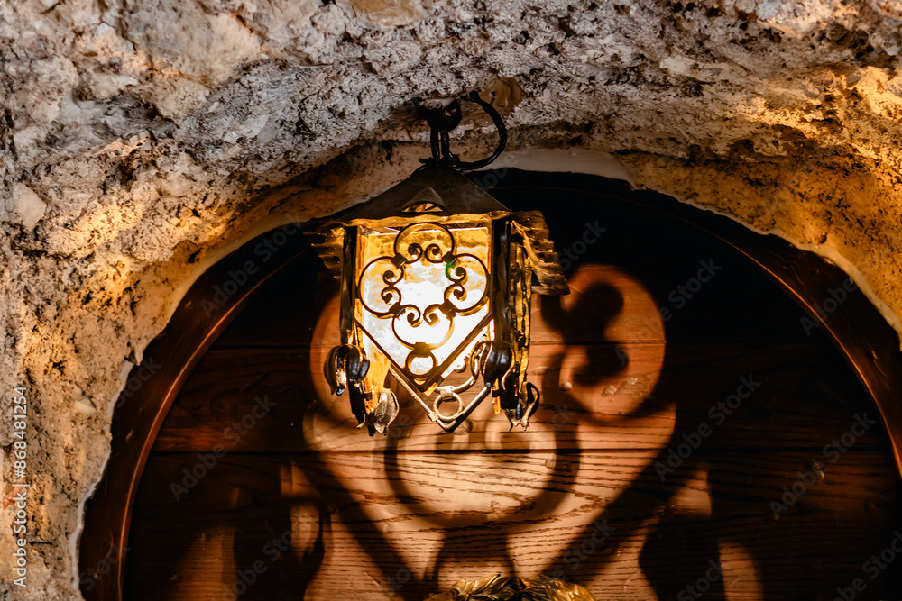 Aged brass light fixture in a stone archway casting intricate shadows, creating vintage elegance
