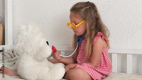 little blond girl play doctor role with white bear toy, home leisure, indoor activity