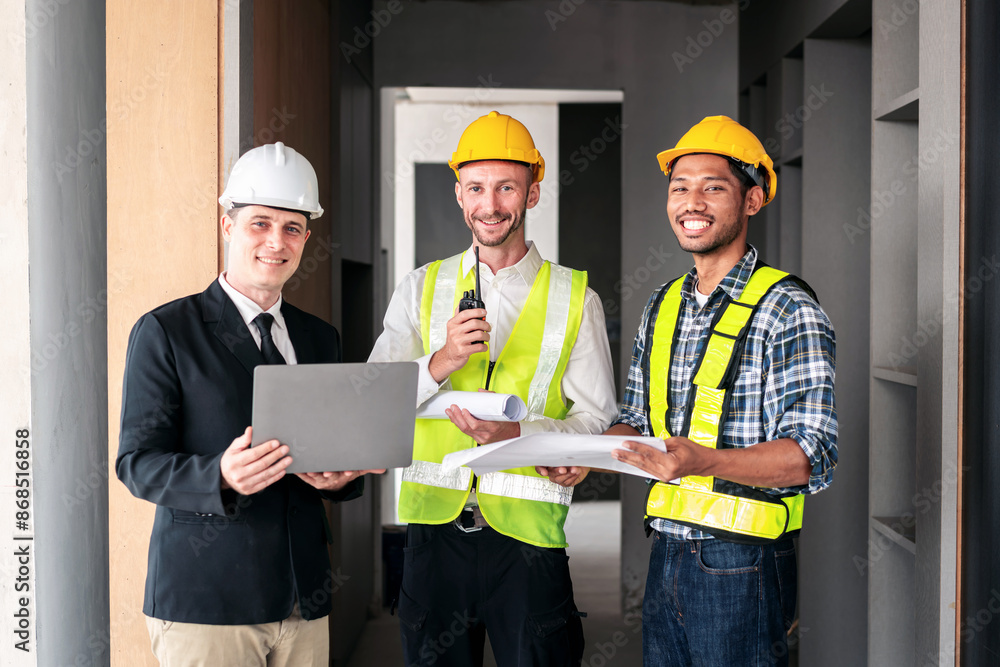 Three men wearing hard hats and safety vests are standing in a hallway