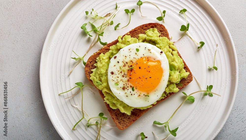 Whole grain toast with mashed avocado, sunny-side-up egg, microgreens on a white ceramic plate. Healthy breakfast. Whole grain toast with mashed avocado, sunny-side-up egg, microgreens on a white ceramic plate. Healthy breakfast.