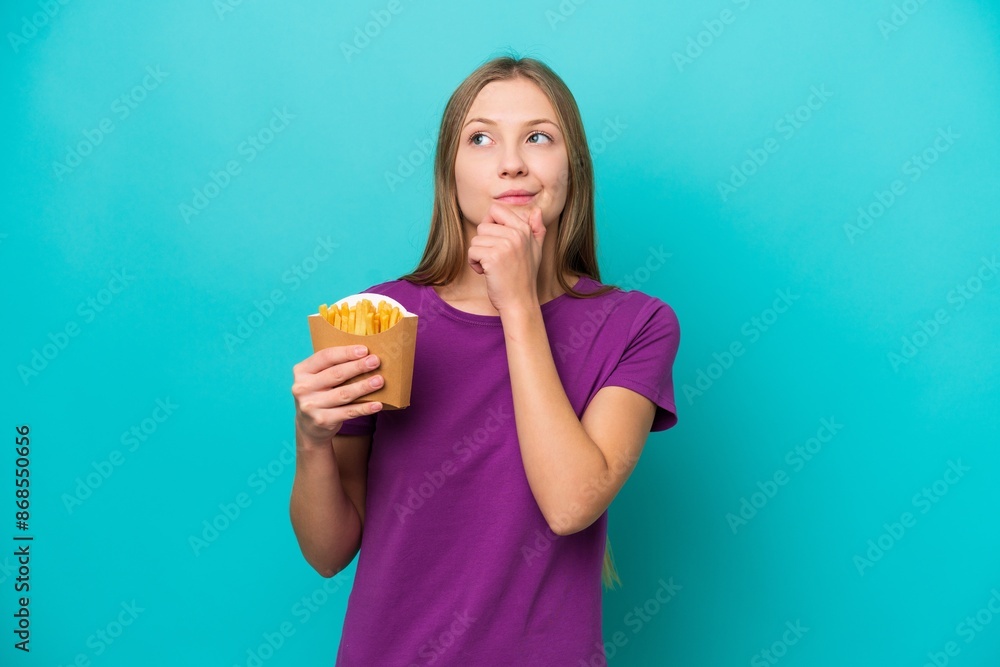 Young Russian woman catching french fries isolated on blue background and looking up Young Russian woman catching french fries isolated on blue background and looking up