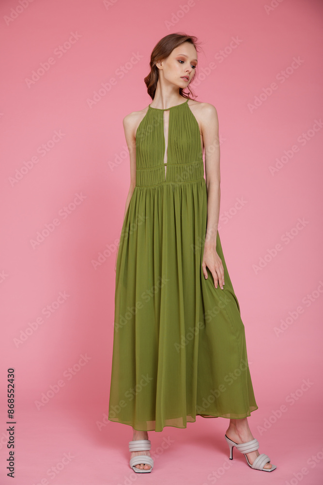 High fashion photo of a beautiful elegant young skinny woman in pretty long green dress posing on pink background. Slim figure. High fashion photo of a beautiful elegant young skinny woman in pretty long green dress posing on pink background. Slim figure.