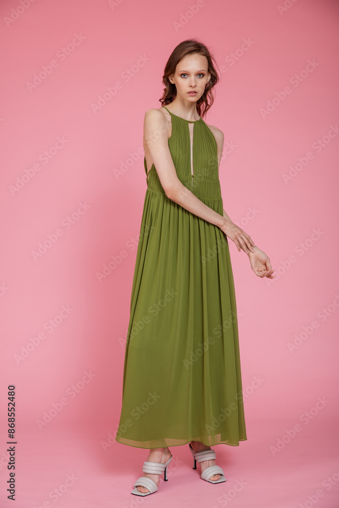 High fashion photo of a beautiful elegant young skinny woman in pretty long green dress posing on pink background. Slim figure. High fashion photo of a beautiful elegant young skinny woman in pretty long green dress posing on pink background. Slim figure.