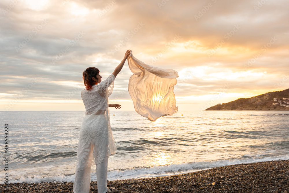 Fototapeta premium A woman stands on a beach holding a white cloth