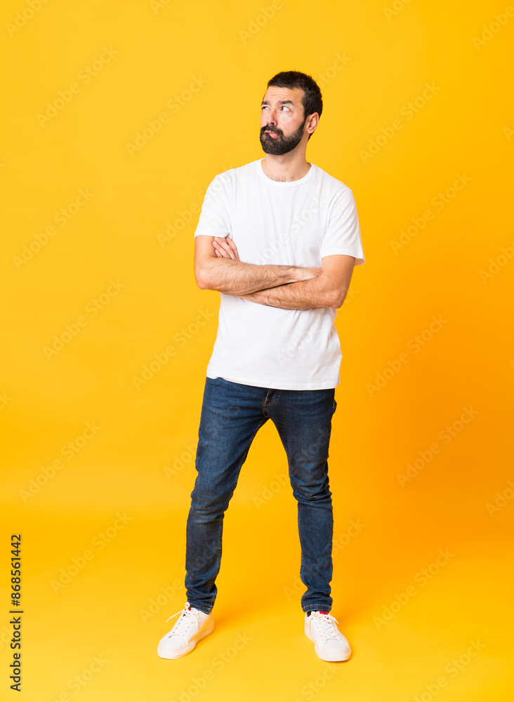 Full-length shot of man with beard over isolated yellow background with confuse face expression Full-length shot of man with beard over isolated yellow background with confuse face expression