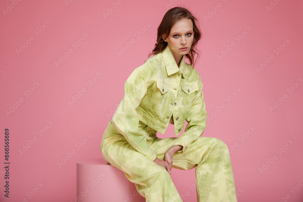 High fashion photo of a beautiful skinny young woman in pretty green military denim jeans pants, jacket, metallic bronze top posing on pink background. Slim figure. High fashion photo of a beautiful skinny young woman in pretty green military denim jeans pants, jacket, metallic bronze top posing on pink background. Slim figure.