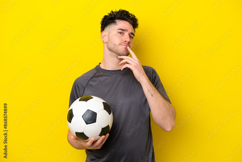 Handsome young football player man isolated on yellow background having doubts while looking up Handsome young football player man isolated on yellow background having doubts while looking up