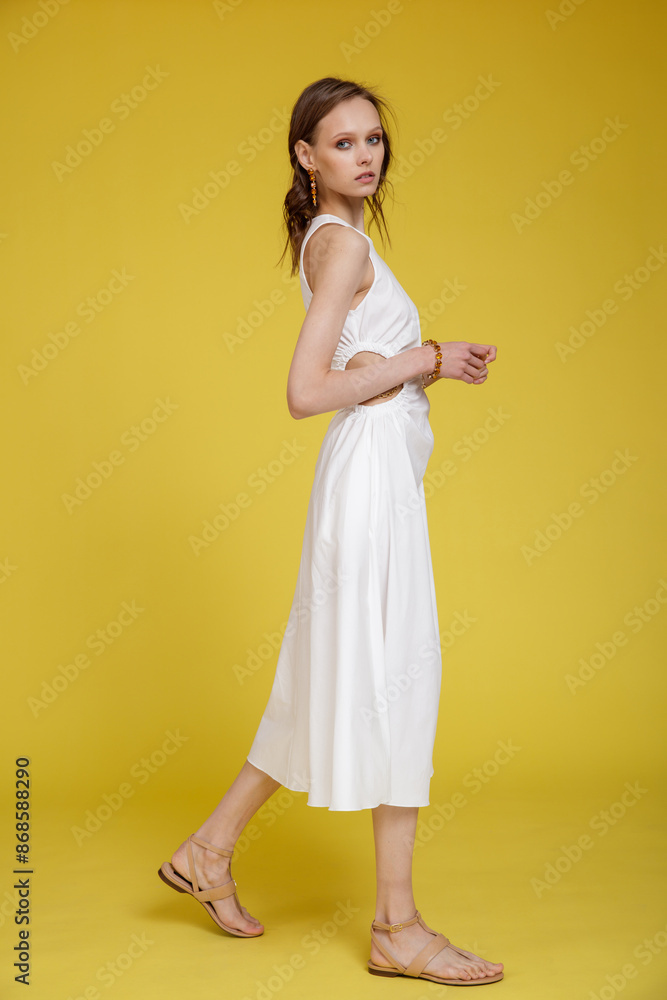 High fashion photo of a beautiful skinny young woman in pretty white dress posing on yellow background. Slim figure. High fashion photo of a beautiful skinny young woman in pretty white dress posing on yellow background. Slim figure.