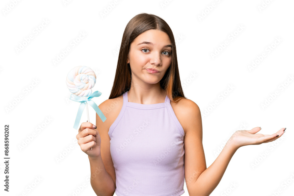 Teenager caucasian girl holding a lollipop over isolated background making doubts gesture while lifting the shoulders Teenager caucasian girl holding a lollipop over isolated background making doubts gesture while lifting the shoulders