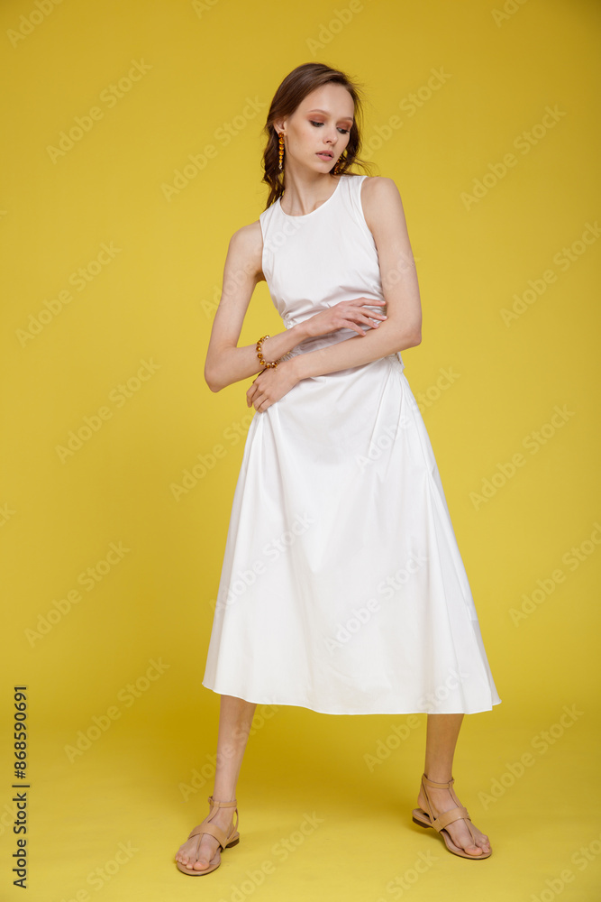 High fashion photo of a beautiful skinny young woman in pretty white dress posing on yellow background. Slim figure. High fashion photo of a beautiful skinny young woman in pretty white dress posing on yellow background. Slim figure.