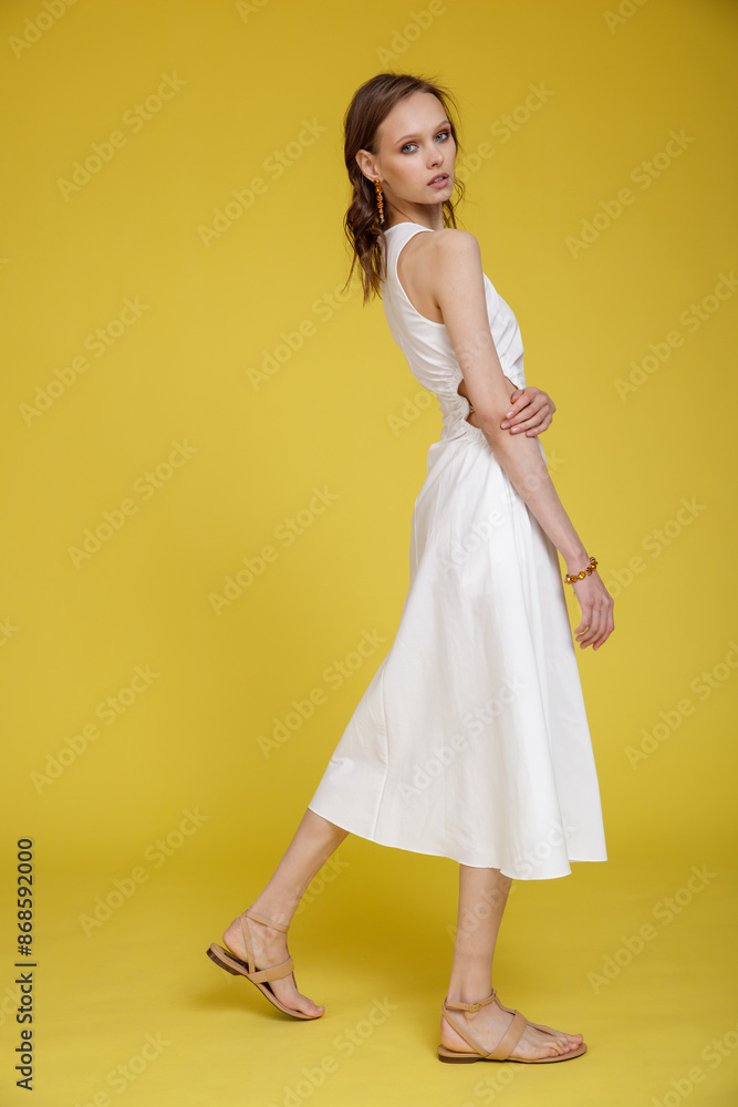 High fashion photo of a beautiful skinny young woman in pretty white dress posing on yellow background. Slim figure. High fashion photo of a beautiful skinny young woman in pretty white dress posing on yellow background. Slim figure.