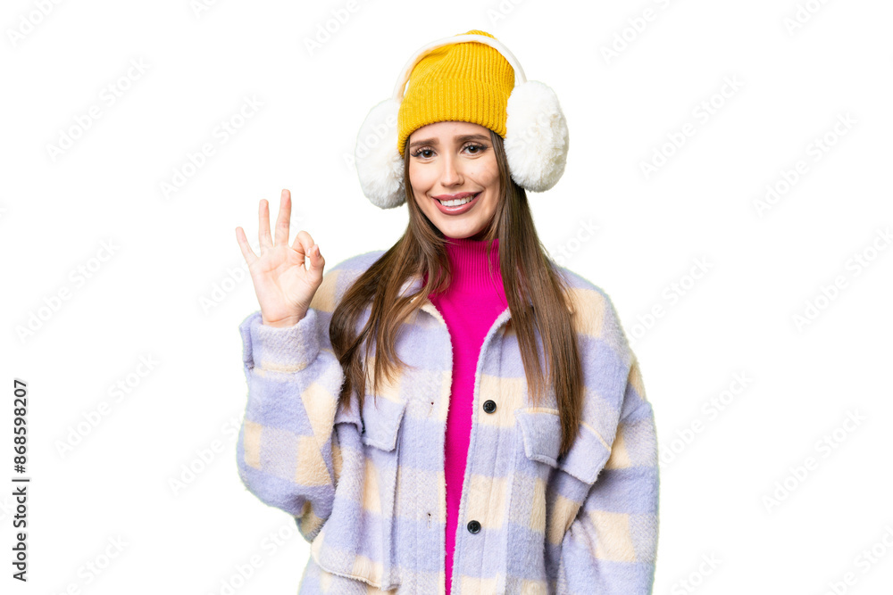 Young woman wearing winter muffs over isolated chroma key background showing ok sign with fingers Young woman wearing winter muffs over isolated chroma key background showing ok sign with fingers