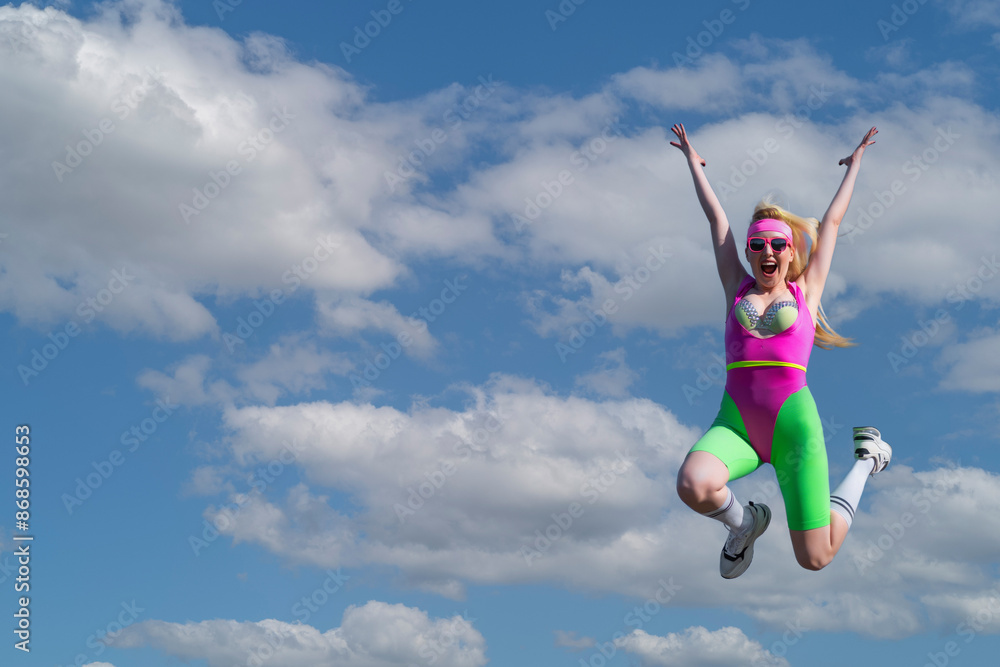 Young beautiful blonde woman in sports shorts, a pink bodysuit and pink sunglasses is doing sports outdoors. Jumping against the sky. Sports, Active lifestyle, sports training, healthy lifestyle Young beautiful blonde woman in sports shorts, a pink bodysuit and pink sunglasses is doing sports outdoors. Jumping against the sky. Sports, Active lifestyle, sports training, healthy lifestyle