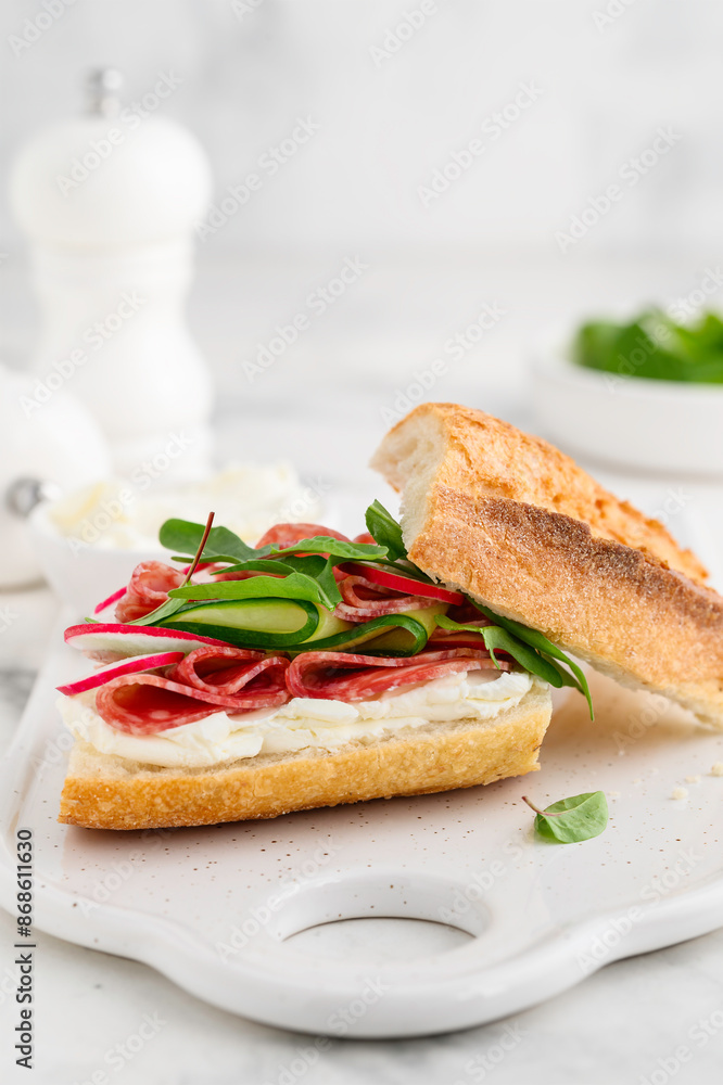 Baguette sandwich with salami, cucumber, radish and herbs on a board. Delicious breakfast, snack. Selective focus Baguette sandwich with salami, cucumber, radish and herbs on a board. Delicious breakfast, snack. Selective focus