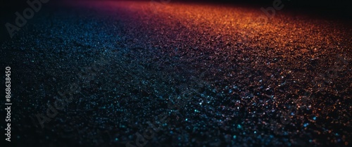 A close up shot of dark asphalt lit by red and blue lights at night, creating a sparkling effect