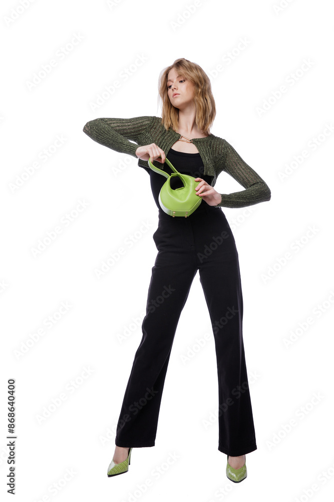 High fashion photo of a beautiful elegant young woman in pretty black denim pants, trousers, top, green short jacket, handbag posing on white background. Slim figure. Blonde