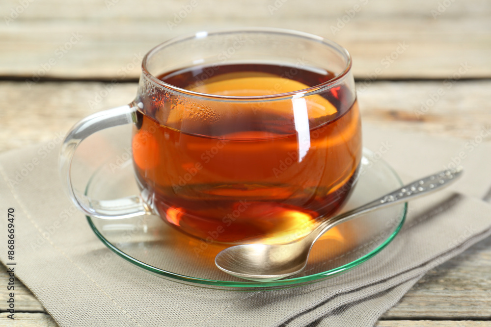 Aromatic tea in glass cup, spoon and napkin on wooden table Aromatic tea in glass cup, spoon and napkin on wooden table