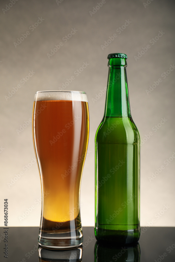 Bottle and glass of beer on table against beige background Bottle and glass of beer on table against beige background