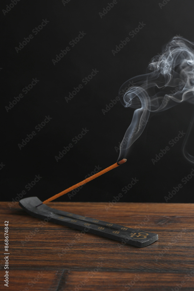 Aromatic incense stick smoldering in holder with Om signs on wooden table Aromatic incense stick smoldering in holder with Om signs on wooden table