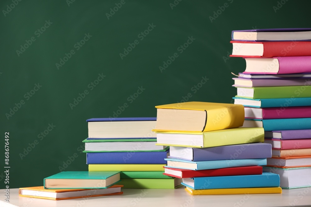 Stacks of many colorful books on white table near chalkboard in classroom. Space for text Stacks of many colorful books on white table near chalkboard in classroom. Space for text