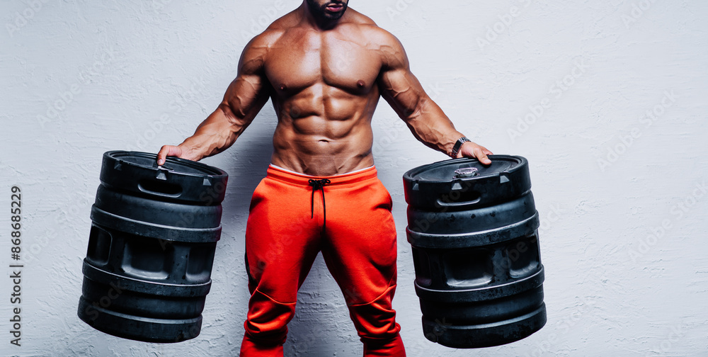 Naklejka premium Young strong man bodybuilder holding big barrels on white wall background