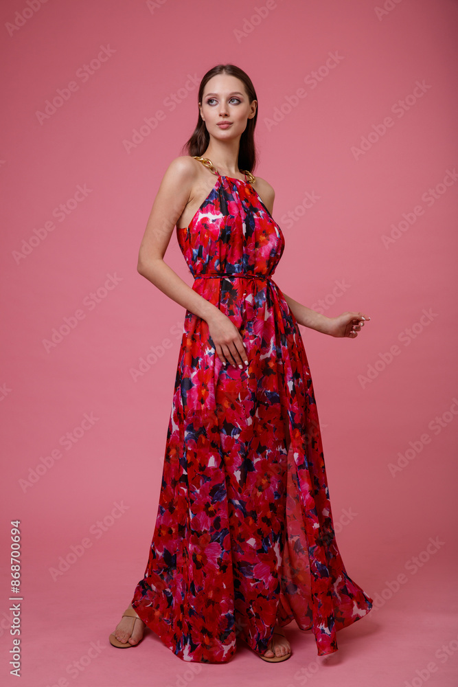 High fashion photo of a beautiful elegant young woman in pretty long dress with floral pattern posing on pink background. Slim figure. High fashion photo of a beautiful elegant young woman in pretty long dress with floral pattern posing on pink background. Slim figure.