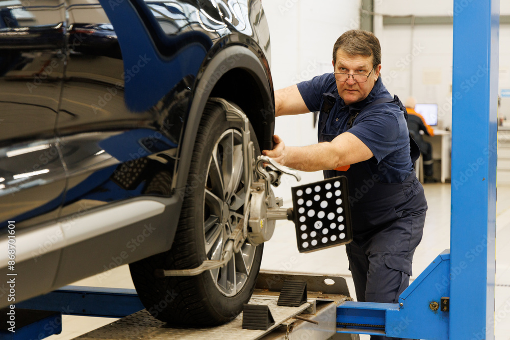 A professional experienced mechanic sets the wheel alignment equipment on a car wheel A professional experienced mechanic sets the wheel alignment equipment on a car wheel