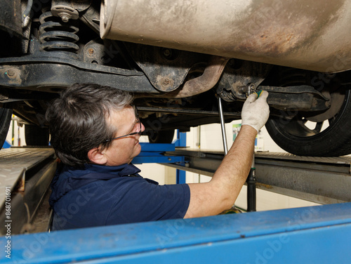 An adult professional mechanic at a car service repairs wheel alignment and adjusts camber bolts