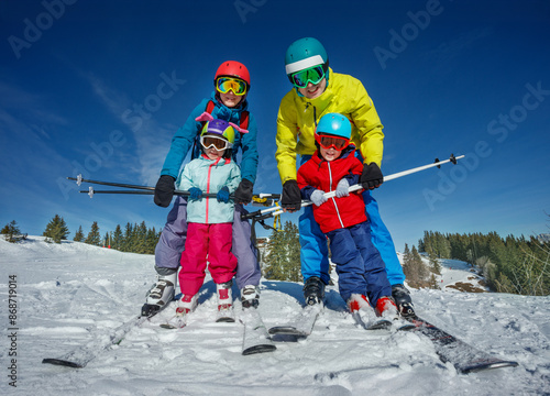 Parents teach kids to ski hold between legs in snowy mountains photo