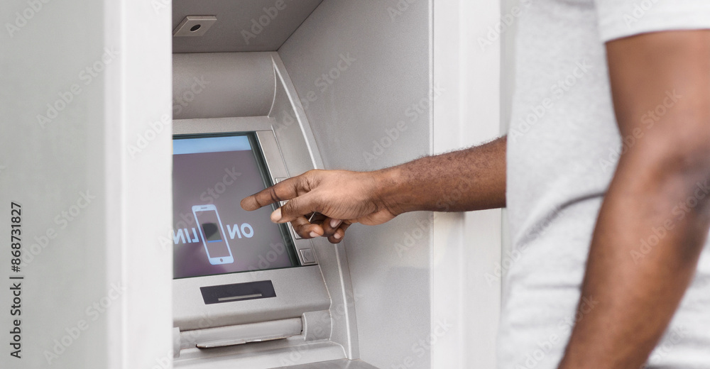 A man uses an ATM machine, pointing his finger at the screen. A man uses an ATM machine, pointing his finger at the screen.
